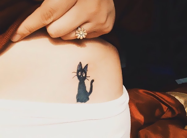 Line art cat tattoo on a person's side, featuring a simple and cute black cat design.