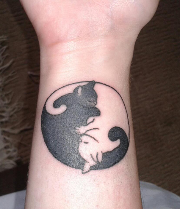 Simple cat tattoo design in line art style on a wrist, featuring two intertwined cats.