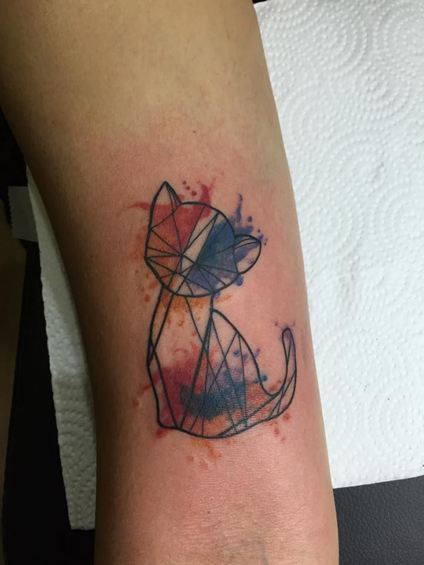 Geometric line art cat tattoo with watercolor style on forearm.