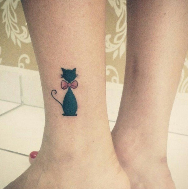 Line art cat tattoo design featuring a black cat with a pink bow on an ankle.