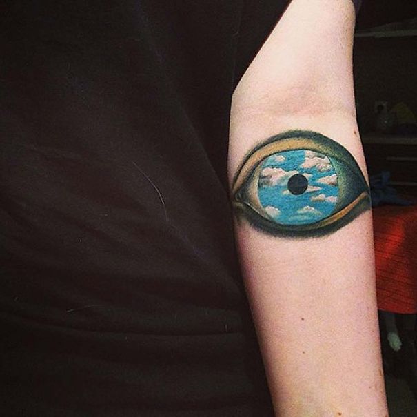 Picasso-inspired tattoo of an eye with a sky and clouds design on a person's arm.