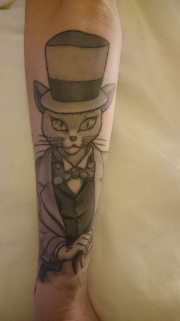 Studio Ghibli tattoo of a dapper cat with a top hat and suit on forearm.