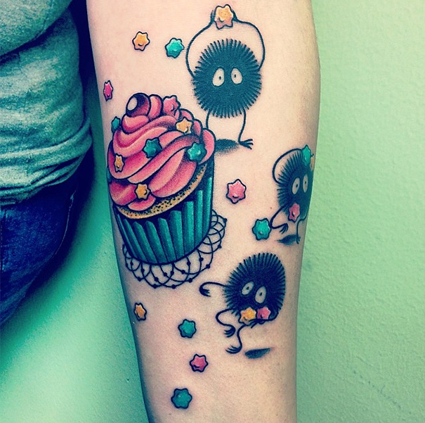 Studio Ghibli tattoo with soot sprites and colorful stars surrounding a cupcake on forearm.