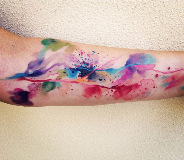 Colorful watercolor tattoo on an arm, featuring vibrant splashes by Czech artist specializing in exquisite designs.