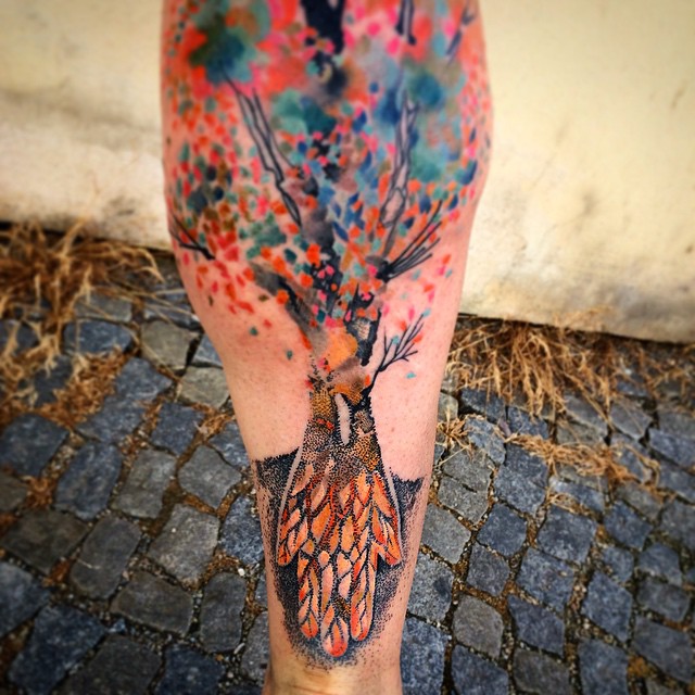 Colorful watercolor tattoo by Czech artist Ondrash on a cobblestone background, showcasing vibrant artistry.