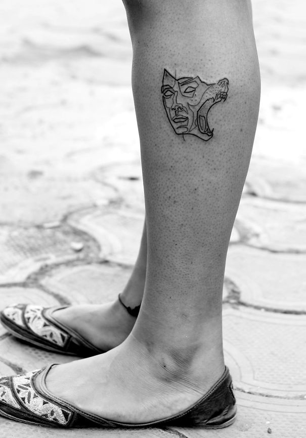Minimalist book-inspired tattoo on a person's calf, combining a face and animal design.