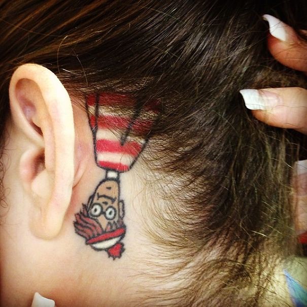 Tattoo of book character behind ear for bookworms, featuring red and white striped hat.