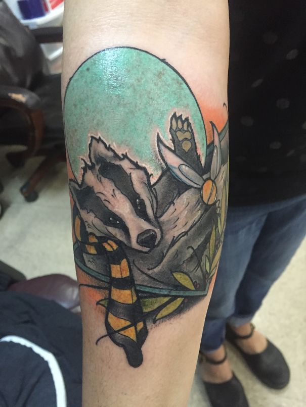 Forearm tattoo of a badger with a striped scarf, inspired by a book, for bookworms.