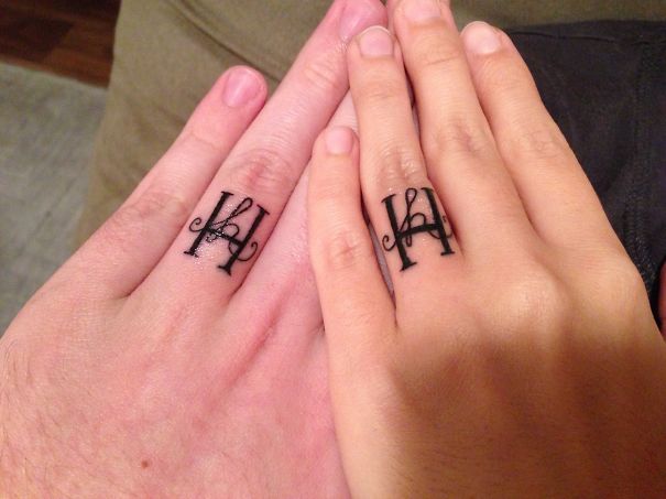 Matching wedding tattoos on couple's fingers instead of rings, featuring intricate black ink design.