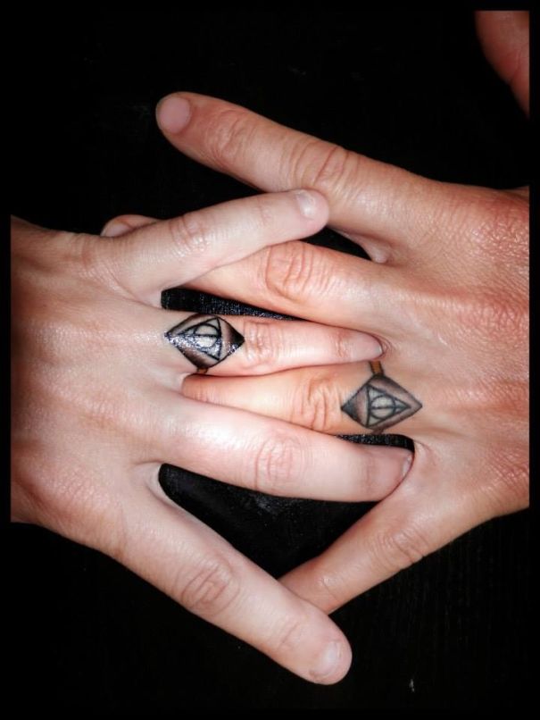 Couple displaying matching wedding tattoos on fingers.