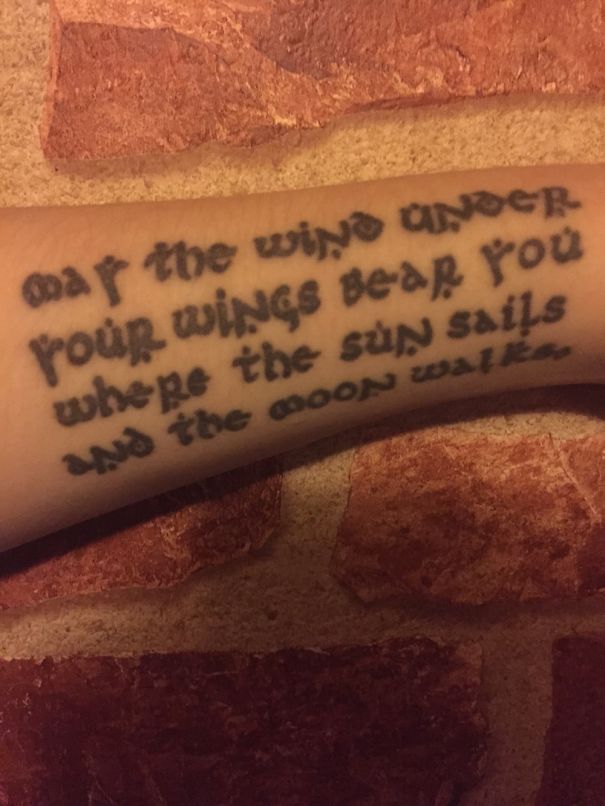 Tattoo of book-inspired quote on arm against a textured brick background.