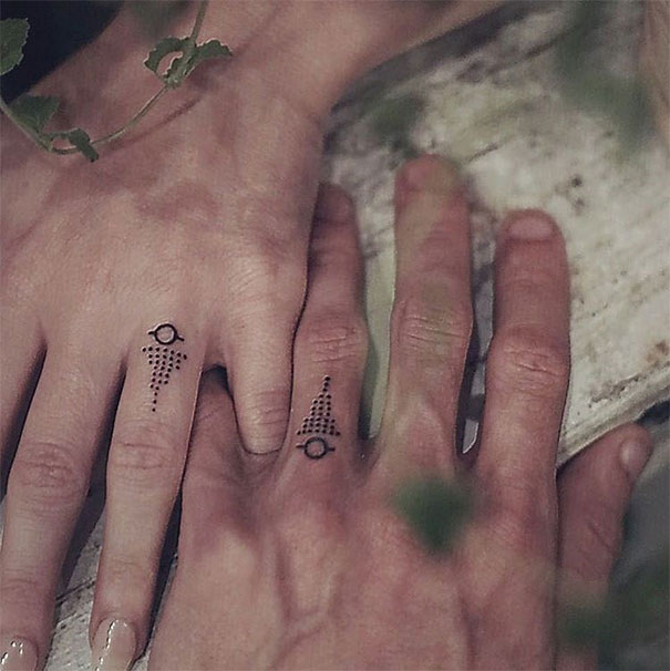 Matching wedding tattoos on couple's ring fingers, featuring minimalistic dot designs.