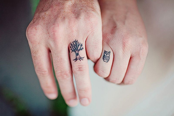 Matching wedding tattoos of a tree and an owl on a couple's fingers, symbolizing commitment.