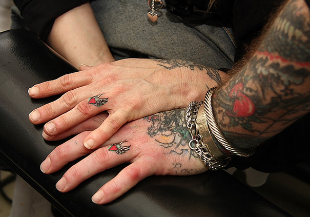 Close-up of a couple's hands with matching wedding tattoos on their ring fingers, symbolizing commitment.