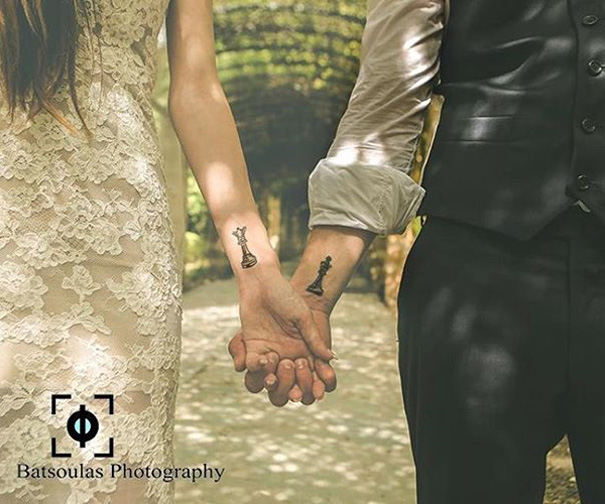 Couple with matching wedding tattoos on arms instead of rings, holding hands in wedding attire.