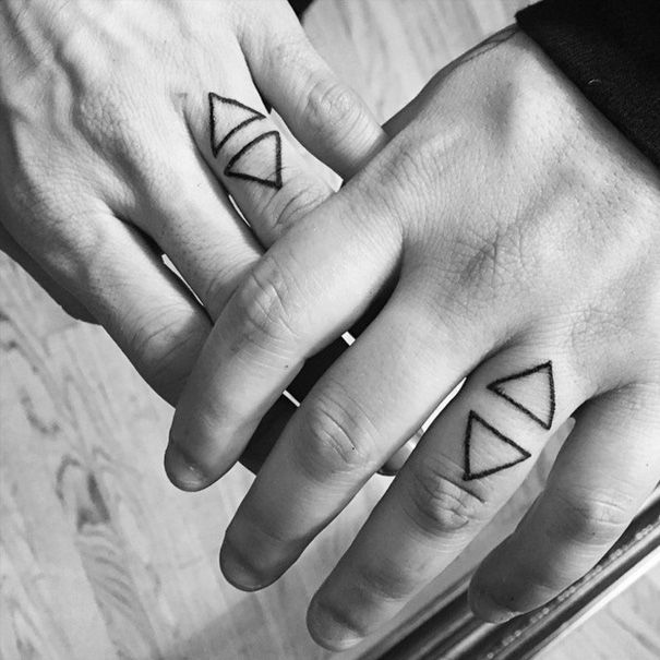 Couple's matching wedding tattoos on fingers, showcasing triangle designs instead of traditional rings.