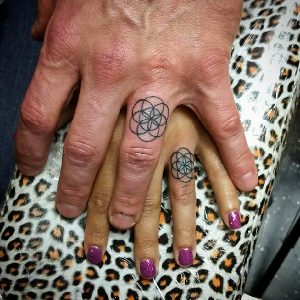 Matching wedding tattoos on ring fingers of a couple's hands, floral geometric design.