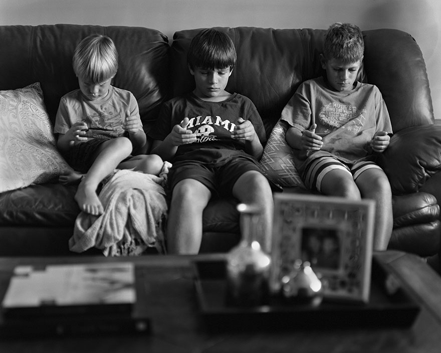 Three boys sitting on a couch with phone-sized voids in their hands, illustrating phone addiction in photography. Three boys sitting on a couch with phone-sized voids in their hands, illustrating phone addiction in photography.