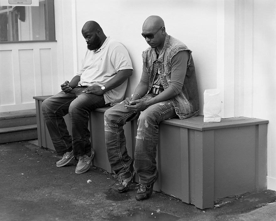 Two men sitting apart on a bench, hands empty, in a black and white photo highlighting phone addiction removal. Two men sitting apart on a bench, hands empty, in a black and white photo highlighting phone addiction removal.
