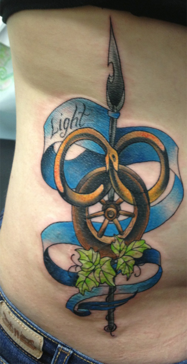Book-inspired tattoo with a snake, vine, and banner featuring the word "Light" on someone's side.