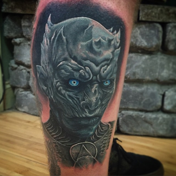 Book-inspired tattoo of a dark fantasy character with glowing blue eyes and detailed armor on the arm.