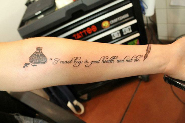 Book-inspired tattoo with a quote and ink bottle design on an arm.