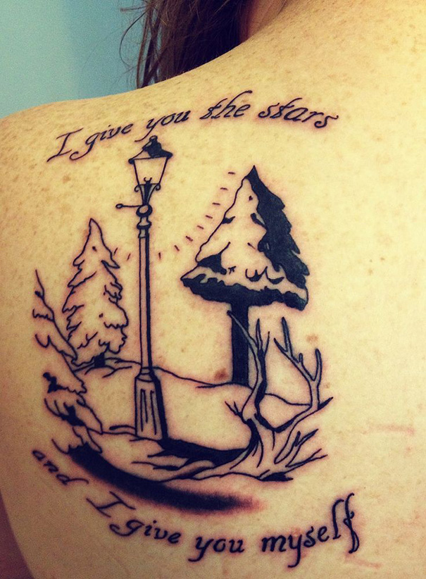 Book-inspired tattoo featuring a quote and illustration of a lamppost and trees on a person's back.