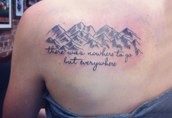 Book-inspired tattoo with mountain design and quote on upper back.