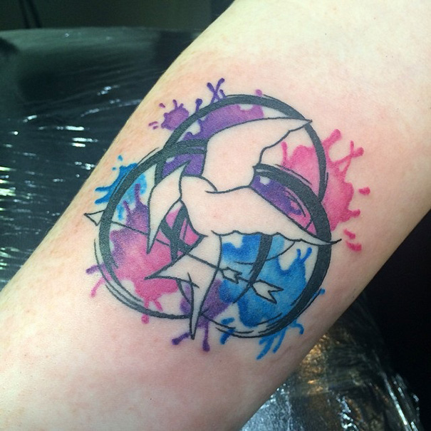 Colorful book-inspired tattoo with a bird and arrow design on a forearm.