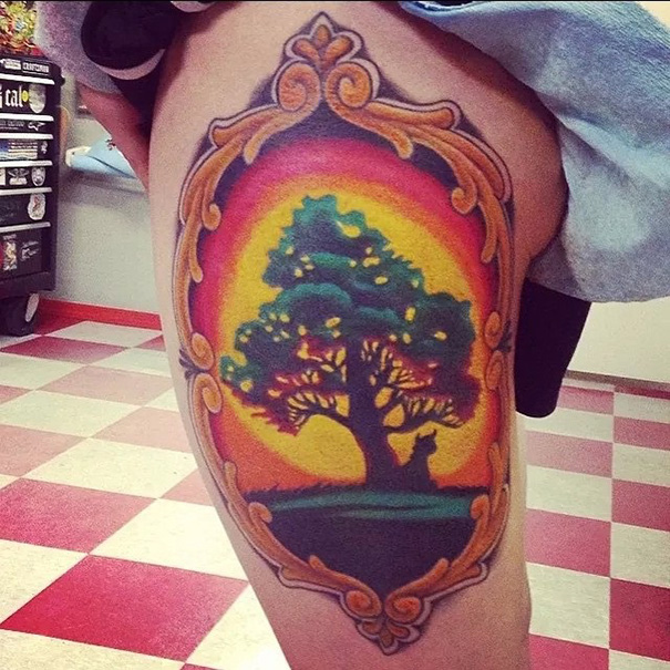 Colorful book-inspired tattoo with a tree and sunset design on a person's thigh.