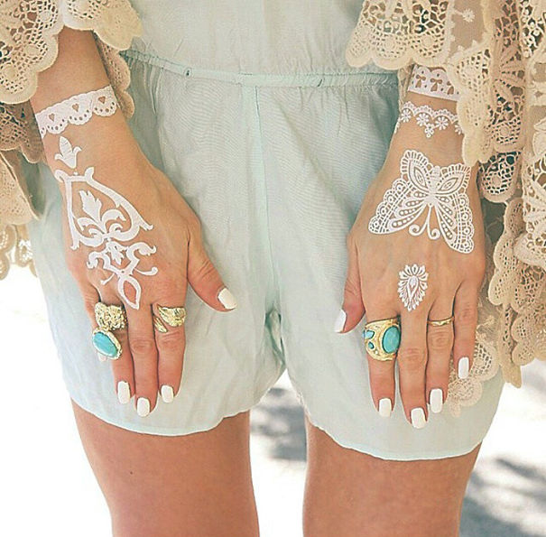 Hands with white henna-inspired tattoos resembling elegant lace, adorned with rings and manicured nails.