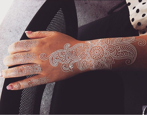 White henna-inspired tattoo on hand, resembling elegant lace with intricate floral patterns.