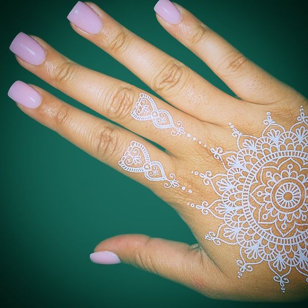 White henna-inspired tattoo on hand, resembling elegant lace, with intricate patterns over fingers and back of the hand.