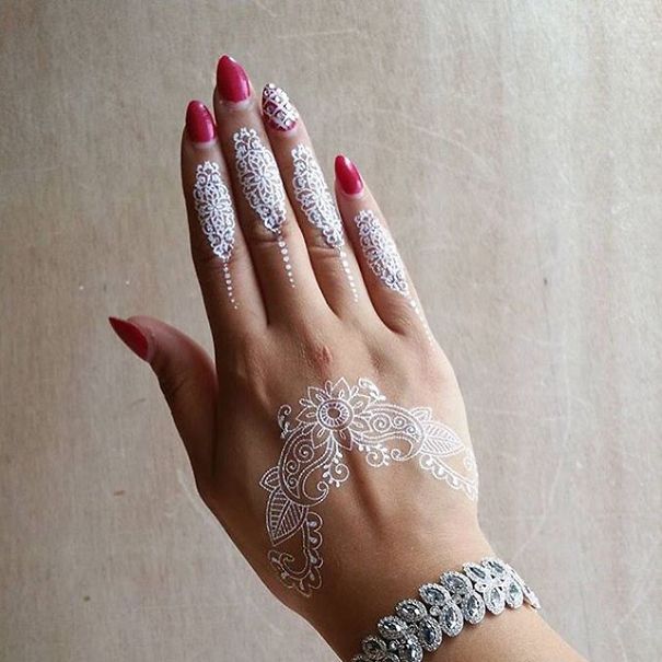 White henna-inspired tattoo on a hand, resembling elegant lace designs with intricate patterns.