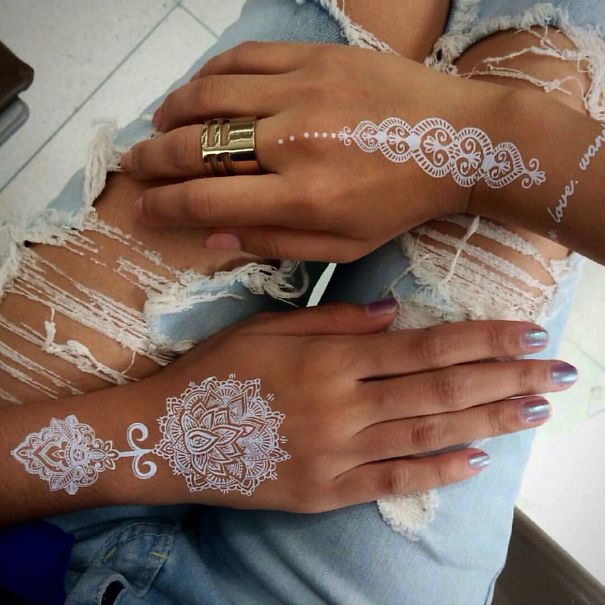 White henna-inspired tattoos on hands, resembling elegant lace, with intricate designs and details.