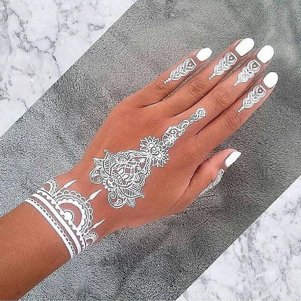 Hand with white henna-inspired tattoos, resembling elegant lace designs.