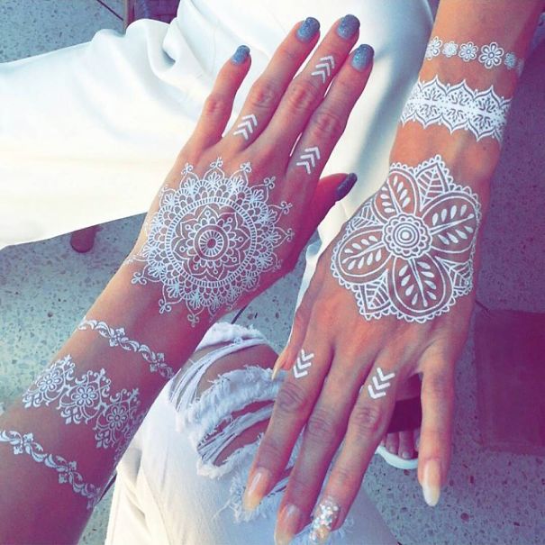 White henna-inspired tattoos on hands, resembling elegant lace patterns.