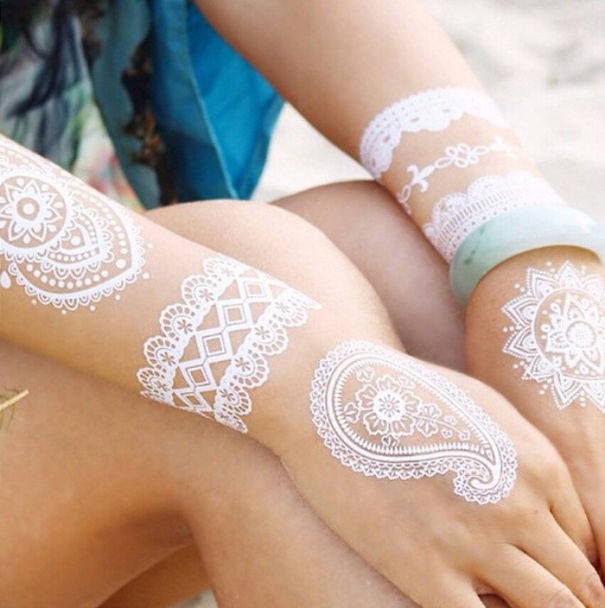 White henna-inspired tattoos on arms, resembling elegant lace patterns.
