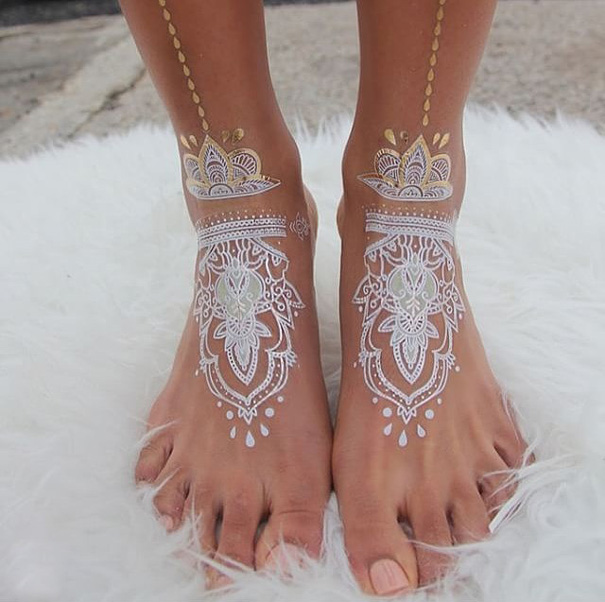 White henna-inspired tattoos on feet resembling elegant lace patterns.
