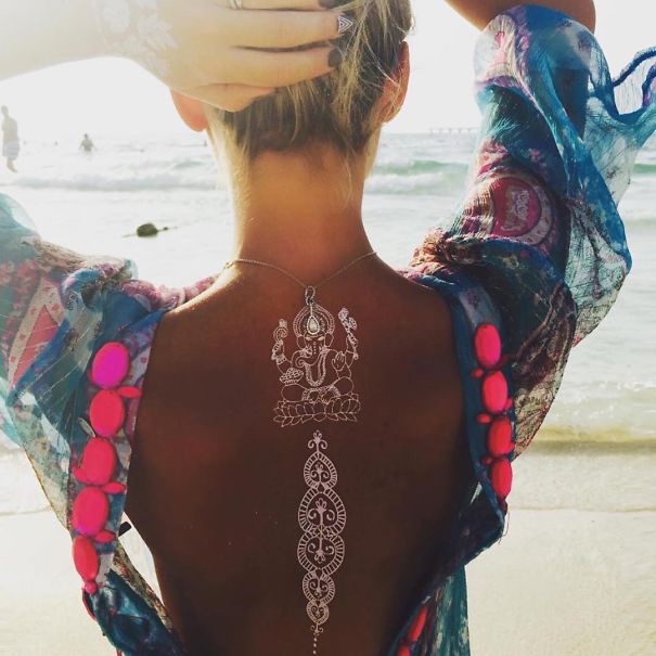 Woman at the beach with white henna-inspired tattoo resembling elegant lace on her back.