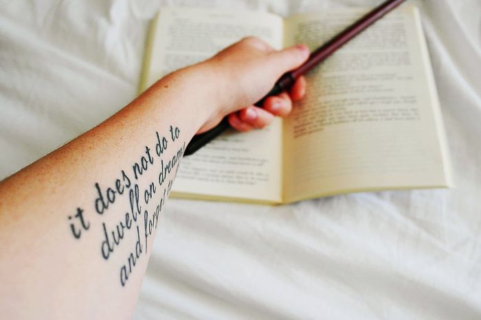 Arm with a Harry Potter tattoo holding a wand over an open book.