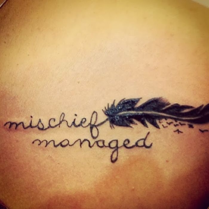 Harry Potter tattoo featuring "mischief managed" script and feather design on skin.