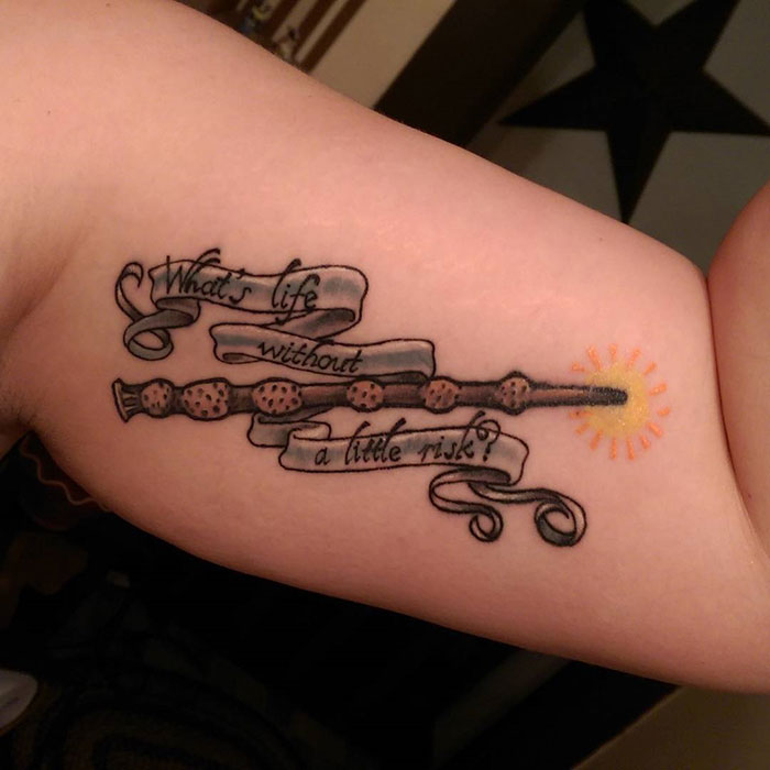 Harry Potter tattoo featuring a wand with the quote "What's life without a little risk?" on a forearm.