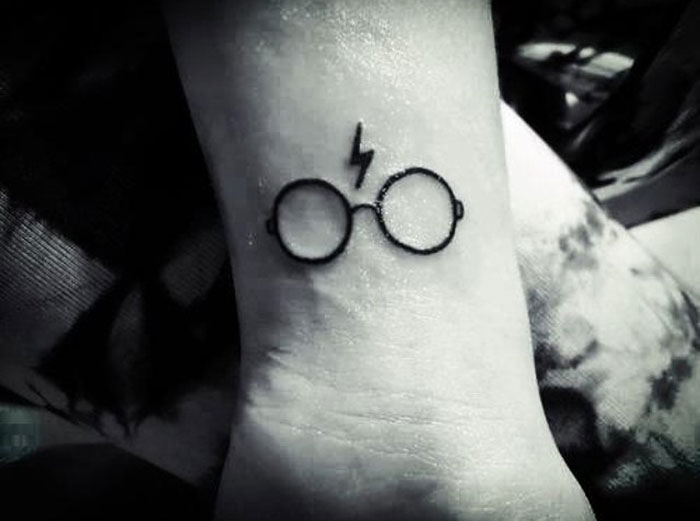 Harry Potter tattoo of glasses and lightning bolt on wrist, showcasing magical design.