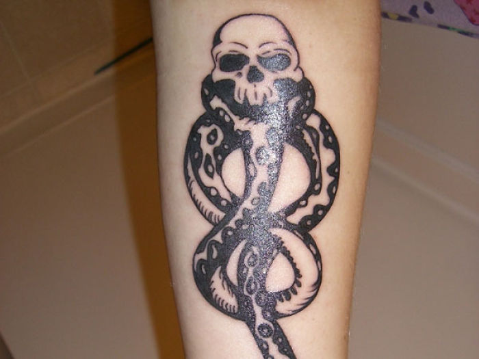 Harry Potter tattoo featuring a skull with a snake intertwined, symbolizing the Dark Mark on the forearm.