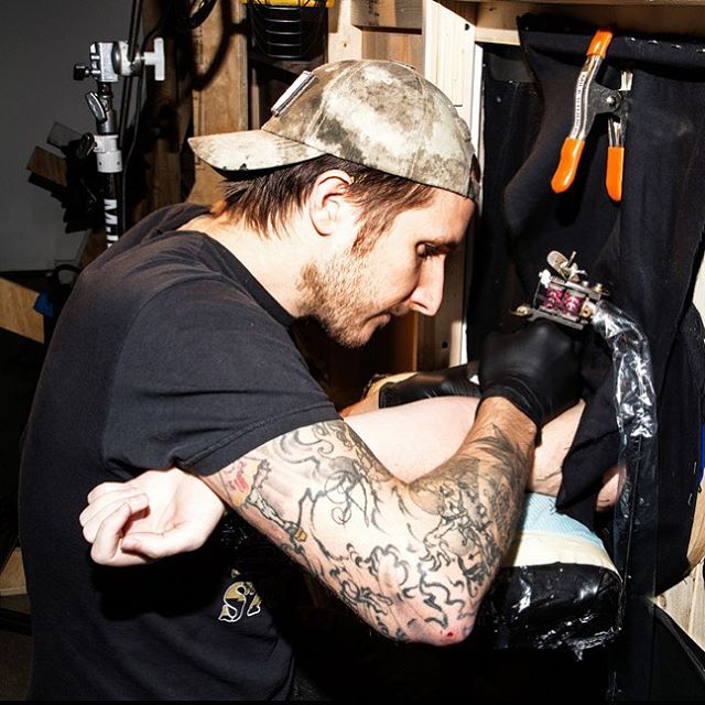 Tattoo artist inking through a hole in a wall, offering surprise tattoos.