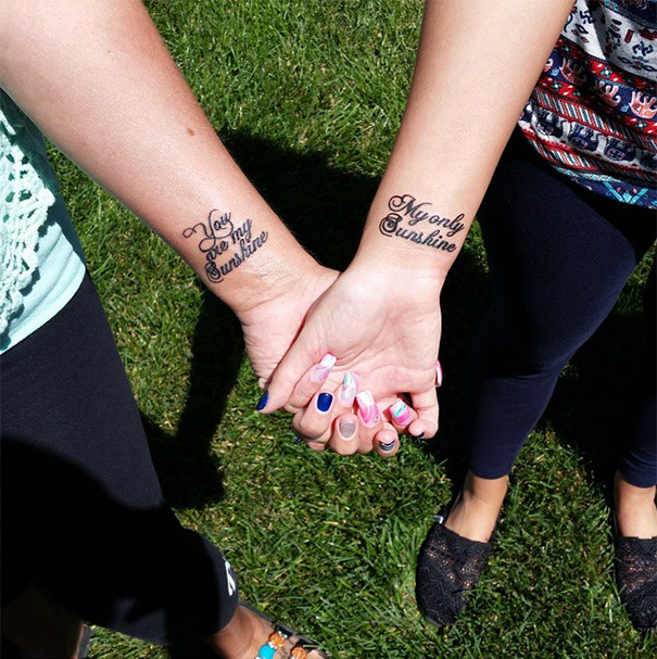 Mother-daughter matching tattoos on wrists, holding hands, symbolizing unbreakable bond.
