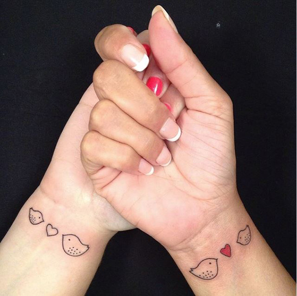 Mother-daughter tattoos of birds and hearts on wrists symbolizing strong bonds.