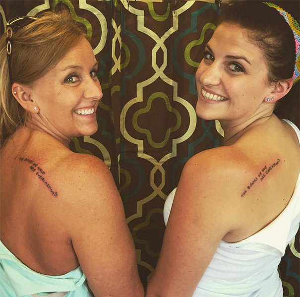 Mother-daughter duo displaying matching phrase tattoos on their backs, symbolizing an unbreakable bond.