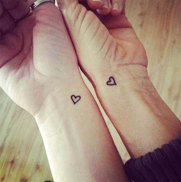 Mother-daughter tattoos with matching small heart designs on their wrists, symbolizing an unbreakable bond.